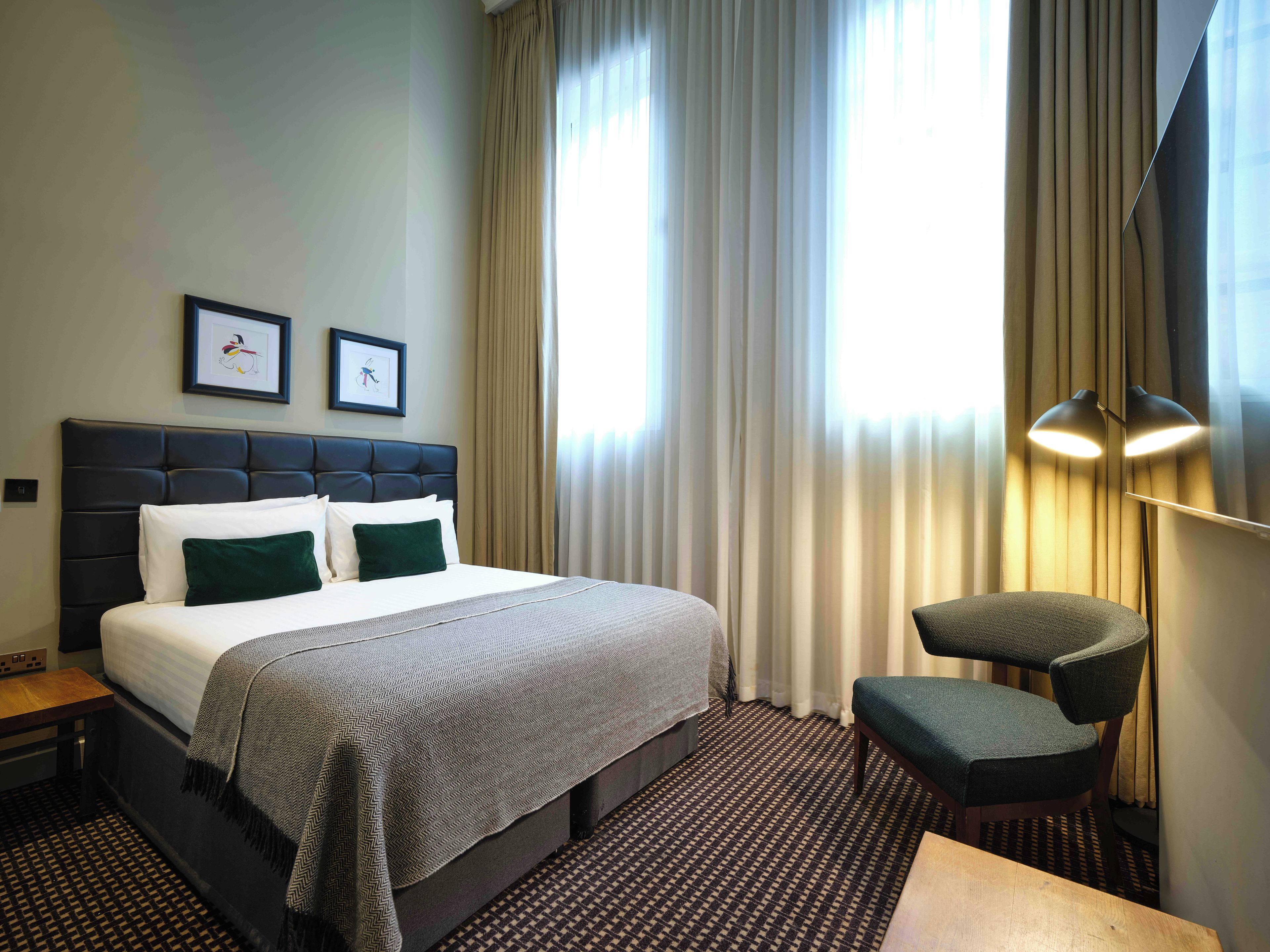 Une chambre d’hôtel avec un lit, une chaise, un bureau et deux tableaux encadrés accrochés au mur.