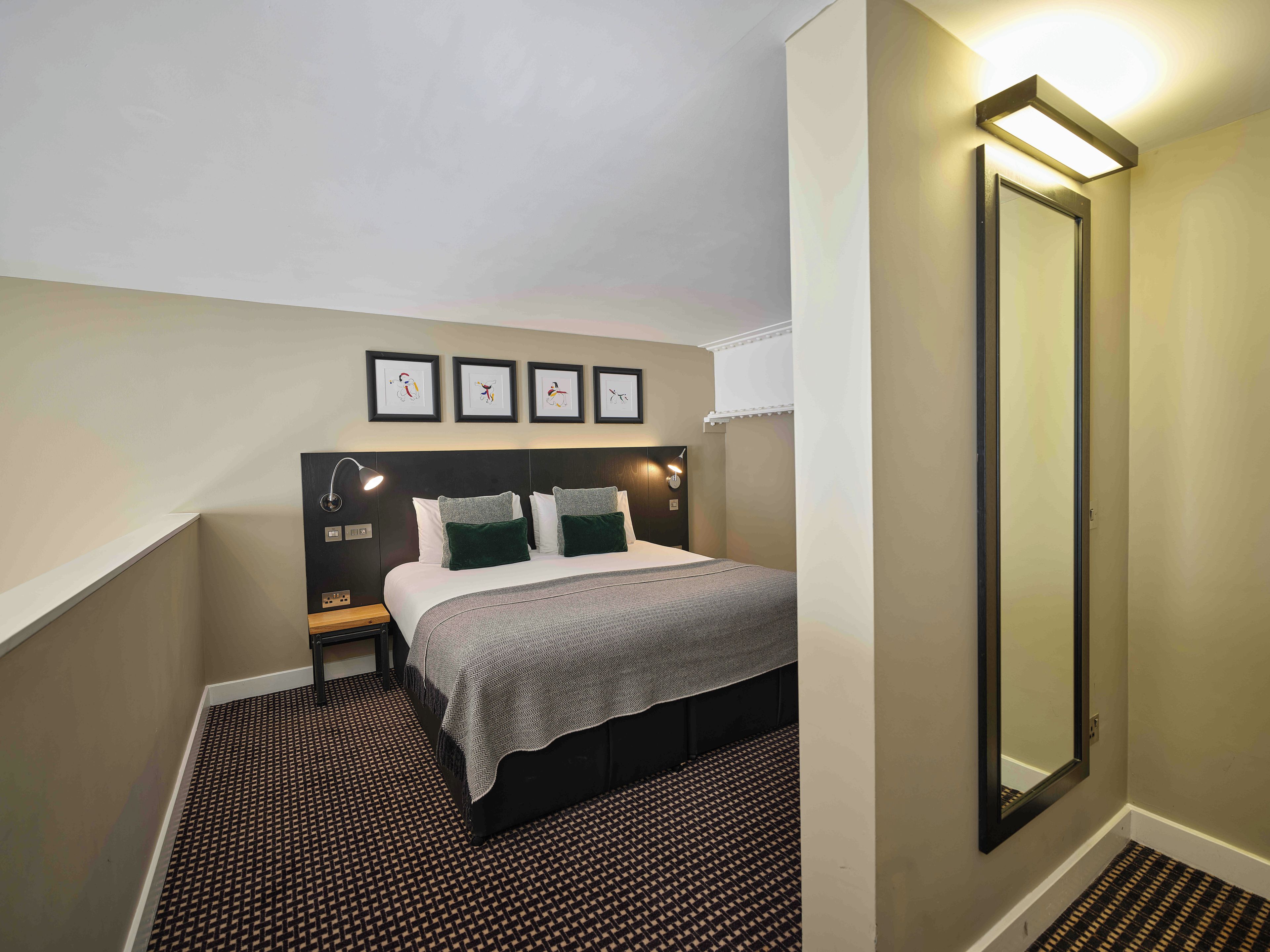 A hotel room with a bed, a nightstand, a wall-mounted mirror, and a ceiling light fixture.