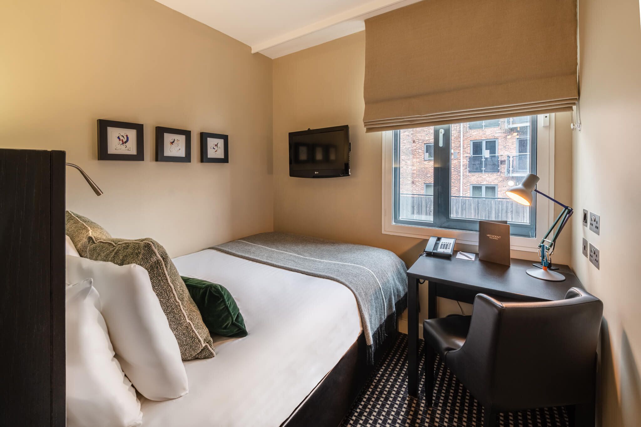 Una habitación de hotel con cama, escritorio, silla, televisión y cuadros en la pared.