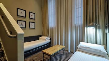 Quarto de hotel com uma cama, um banco, uma escrivaninha e uma escada.