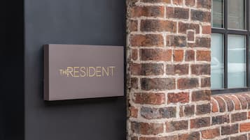 A sign with the word "THRESIDENT" on a dark wall next to a brick wall.