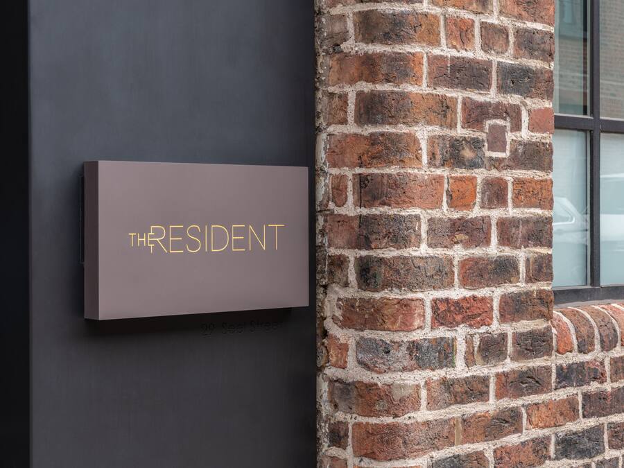 A sign with the word "THRESIDENT" on a dark wall next to a brick wall.