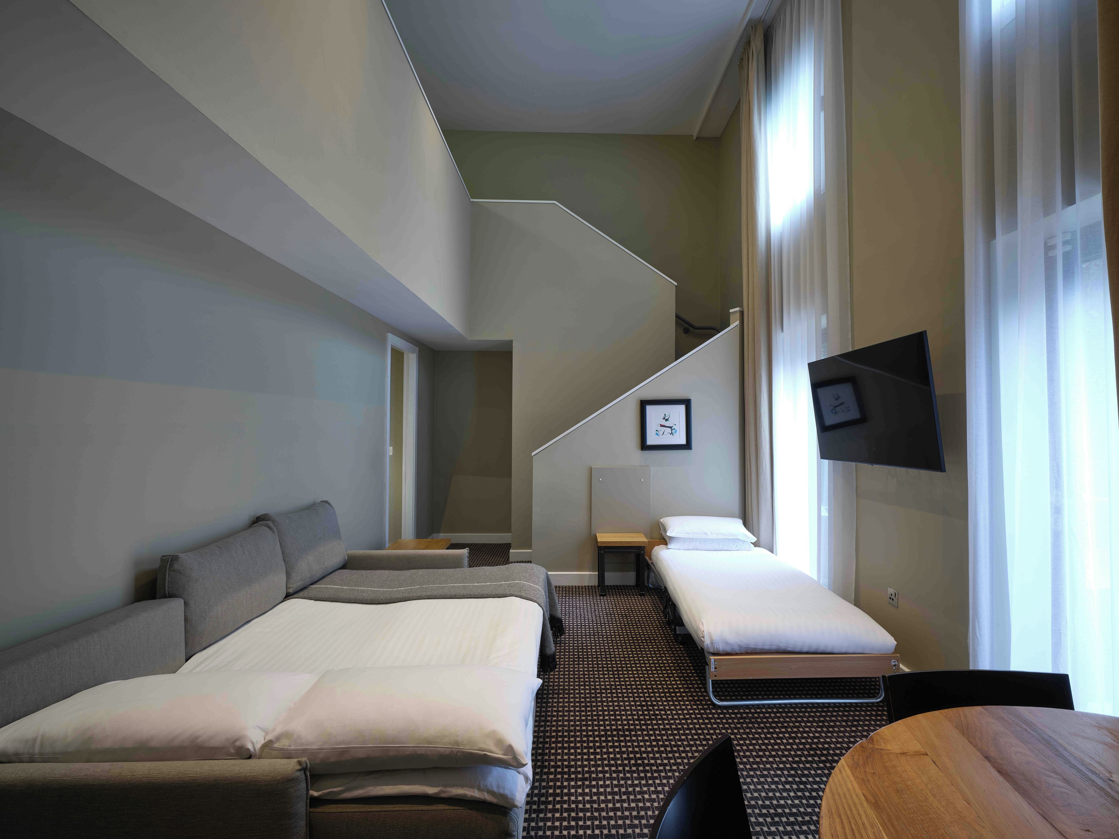 A hotel room with a bed, a sofa, a small table, and a TV mounted on the wall.