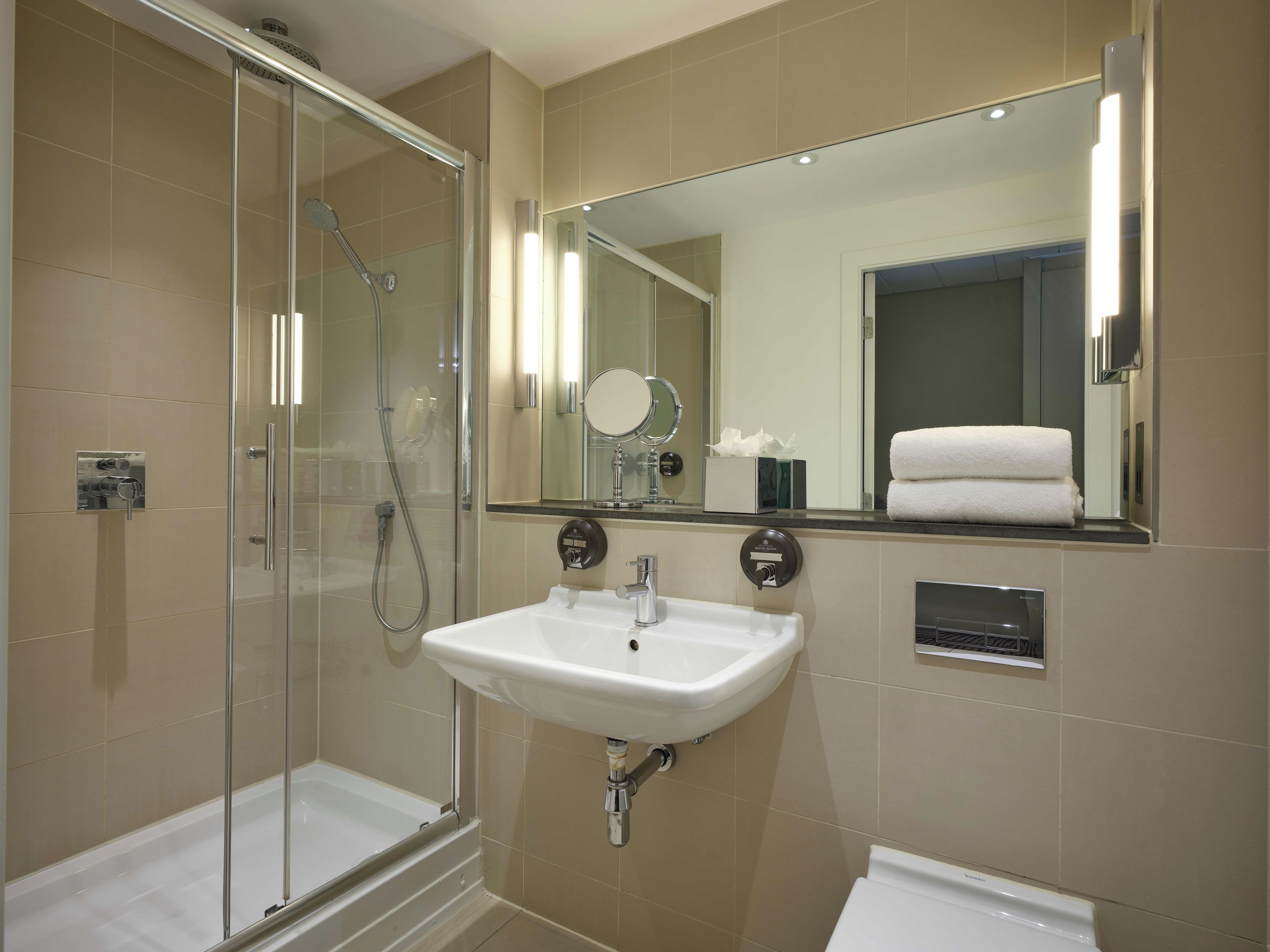 A modern bathroom with a glass-enclosed shower, a white sink, and a large mirror.