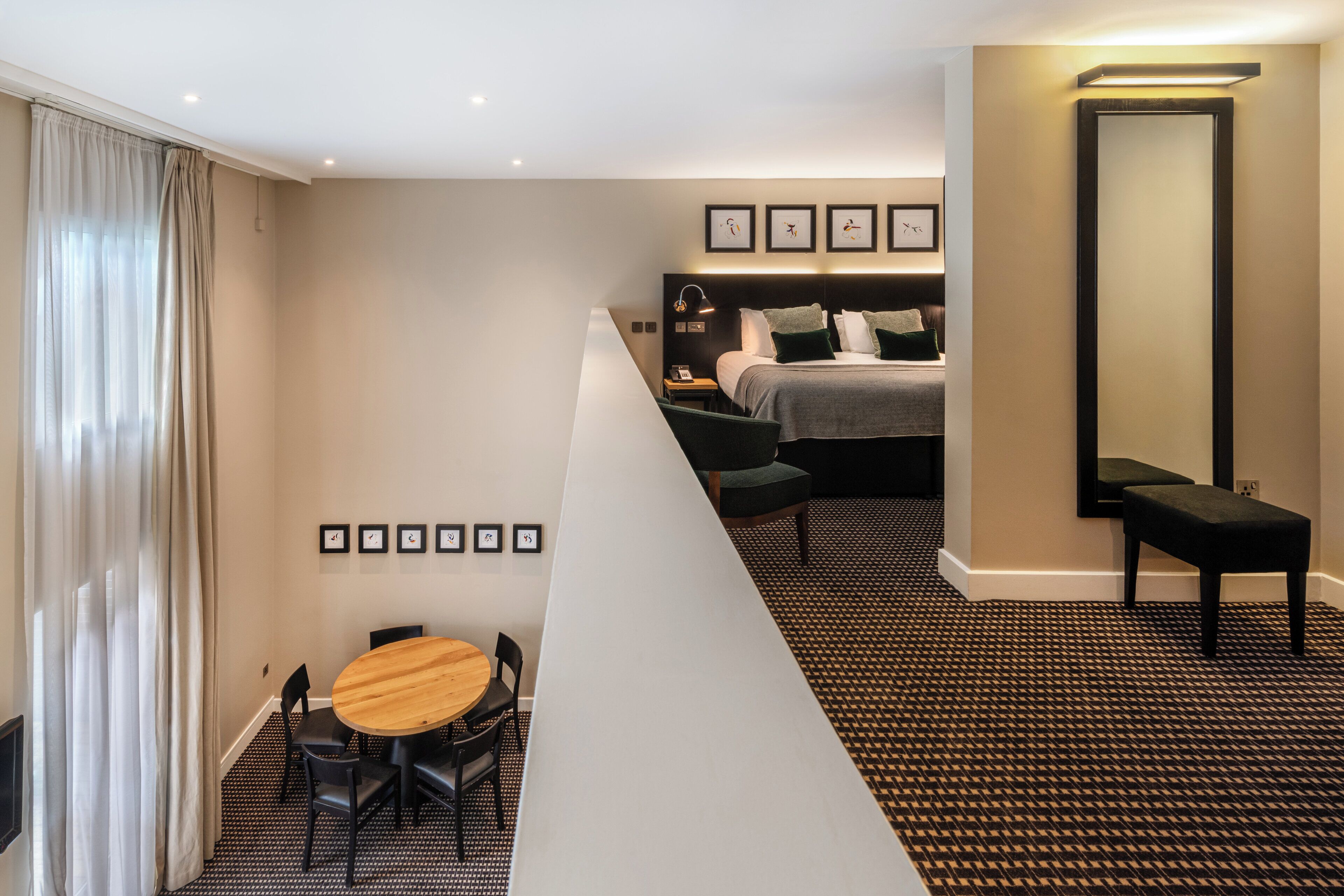 A hotel room with a bed, bedside table, lamp, and a view of the city.