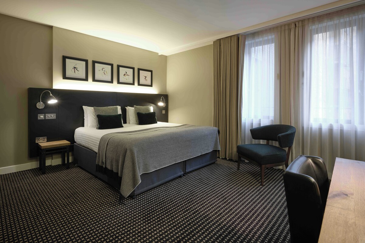 A hotel room with a bed, bedside tables, a desk, and a chair.