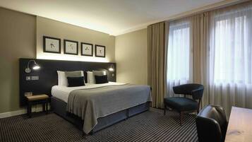 A hotel room with a bed, bedside tables, a desk, and a chair.