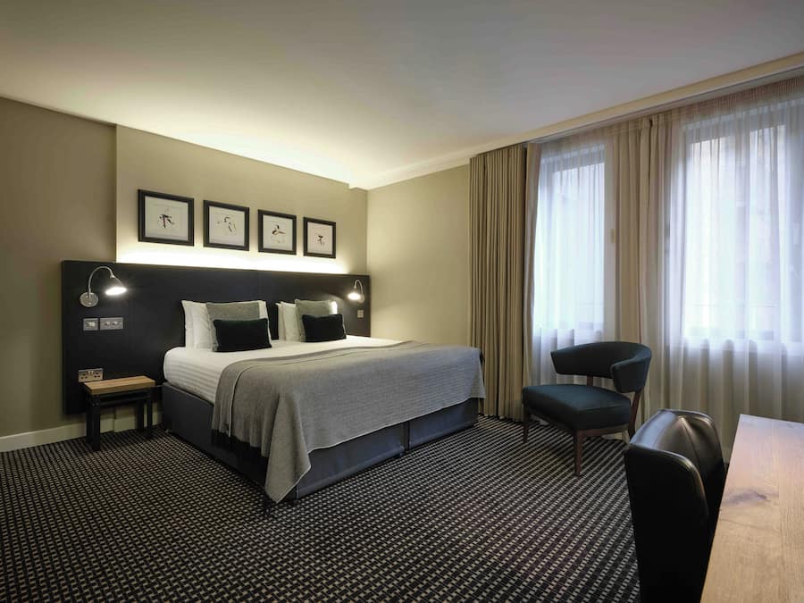 Une chambre d’hôtel avec un lit, des tables de chevet, un bureau et une chaise.