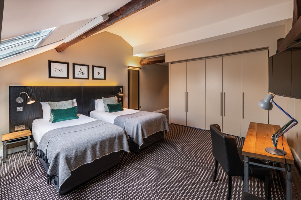 A hotel room with two beds, a desk, and a large wardrobe.