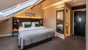 Une chambre d’hôtel moderne dotée d’une lucarne, d’un grand lit avec une couvre-lit grise et d’une tête de lit en bois foncé.