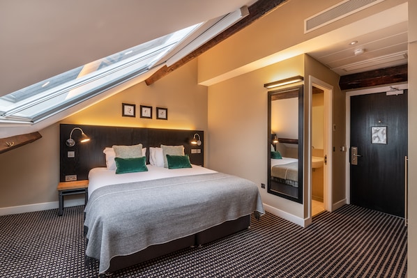 A modern hotel room with a skylight, a large bed with a grey bedspread, and a dark wooden headboard.