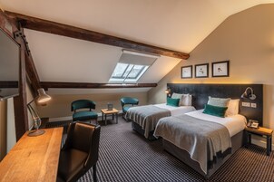Habitación de hotel con dos camas, un escritorio, una silla, una lámpara y un tragaluz.