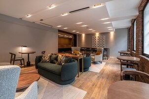 Un área de estar moderna con un sofá, sillones y una mesa de centro. Hay varias mesas y sillas dispuestas para comer o conversar.