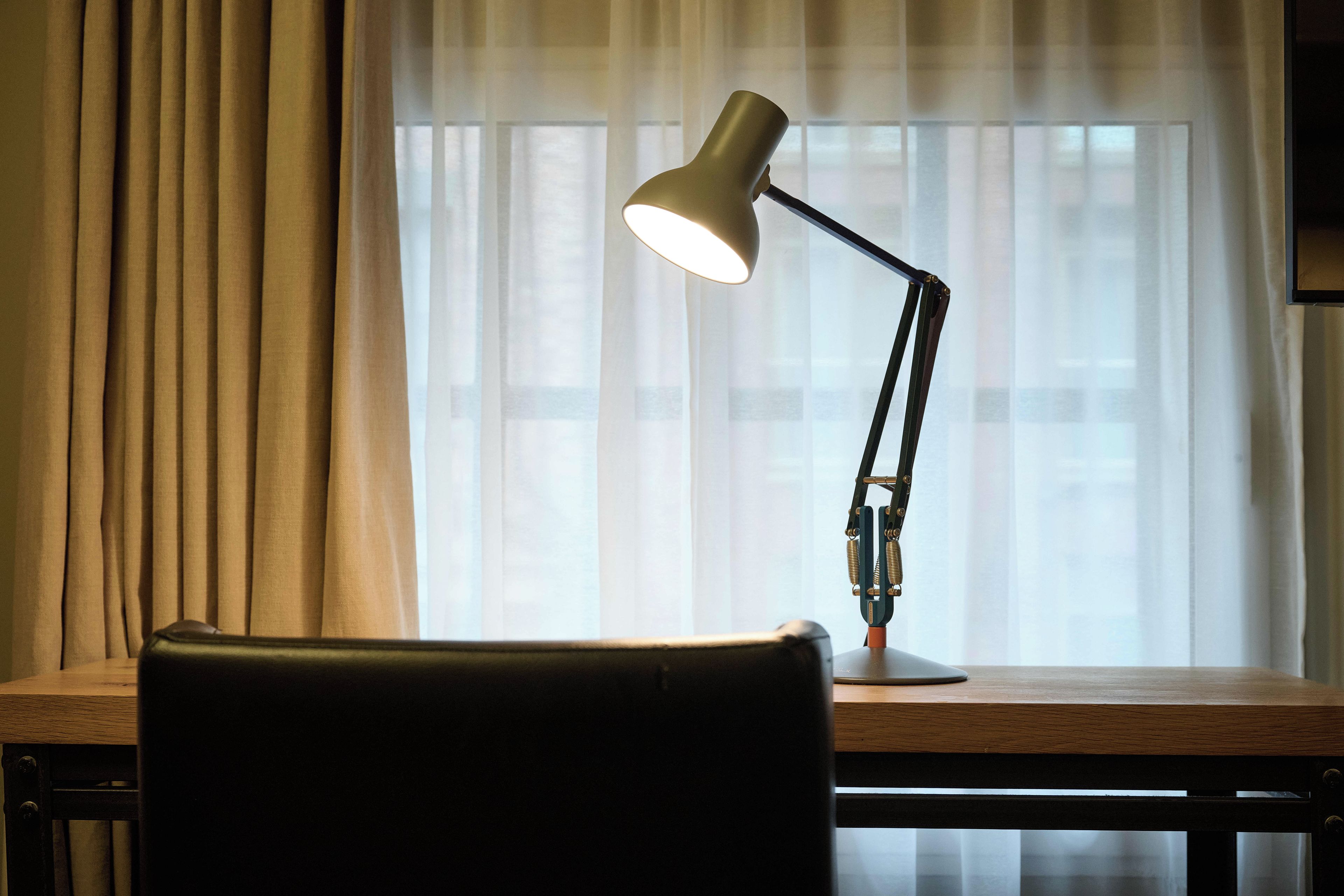Ein Schreibtisch mit Lampe und Stuhl vor einem mit Vorhängen versehenen Fenster.