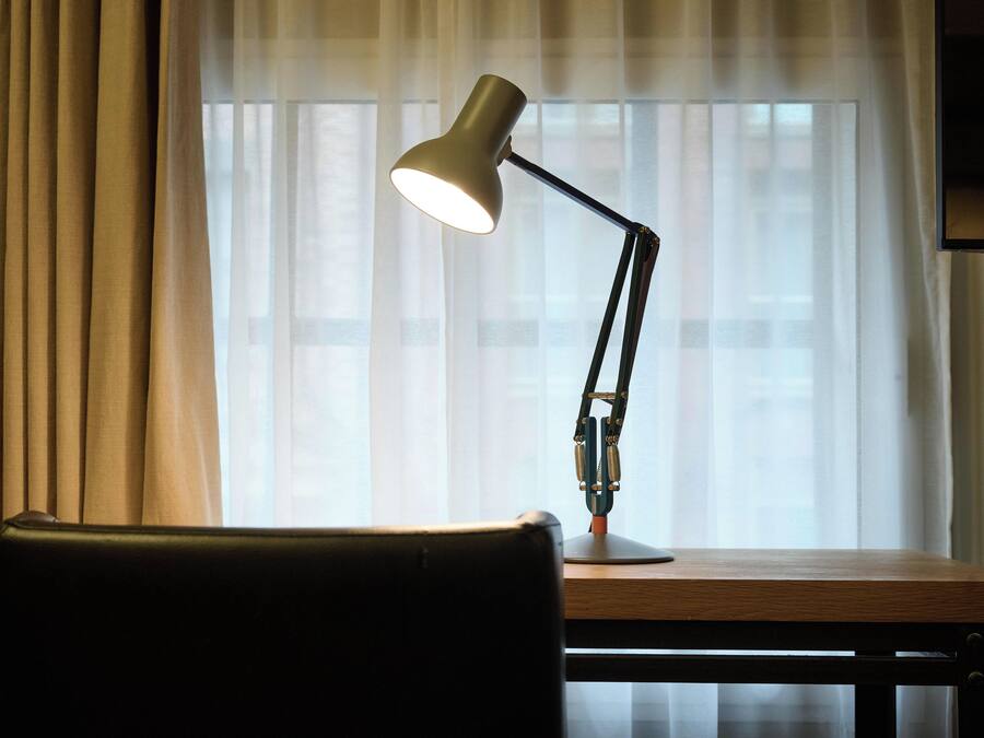 Ein Schreibtisch mit Lampe und Stuhl vor einem mit Vorhängen versehenen Fenster.