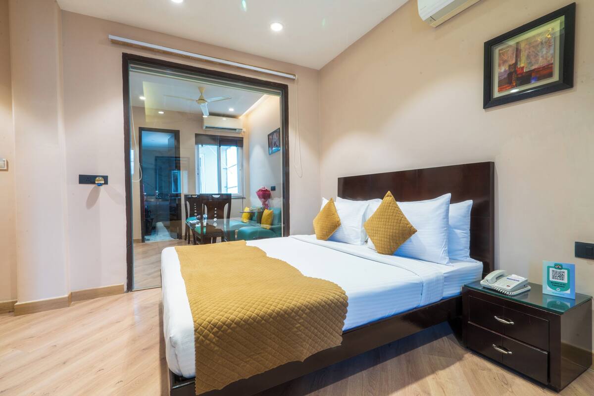 A hotel room with a bed, bedside table, and a glass door leading to a dining area.