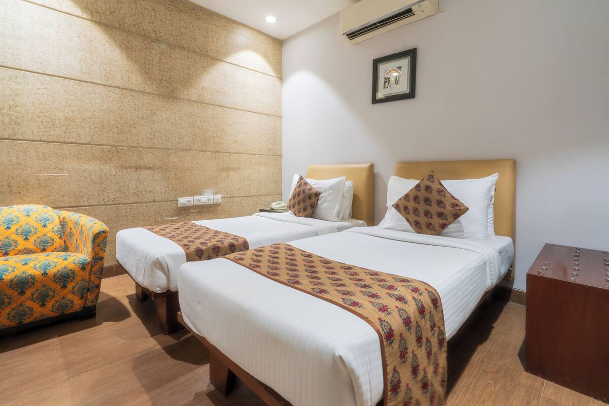 A hotel room with two beds, a chair, and a wooden side table.