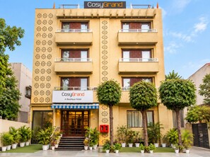 Un hôtel avec une enseigne indiquant « CosyGrand, un hôtel de charme », et une façade symétrique ornée de balcons.