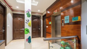 Un hall d’entrée avec des portes en bois, une rambarde en verre et un panneau indiquant l’ascenseur.