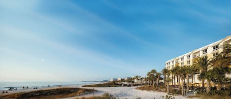 A beachfront hotel with multiple floors, palm trees, and a sandy beach.