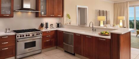 A modern kitchen with a built-in stove, oven, and dishwasher, wooden cabinets, a large island with a sink, and a view of the ocean through the window.
