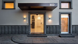 A hotel entrance with a glass door, a sign above the door, and two wall-mounted lights.