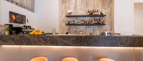 A modern kitchen with a marble countertop, a fruit bowl, and a wine rack above the counter. There are three bar stools in front of the counter.