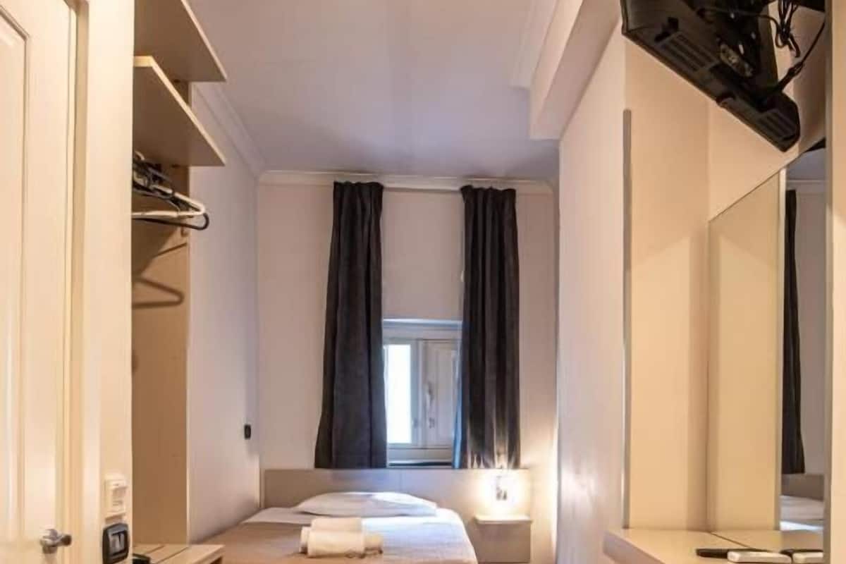 A compact hotel room with a bed, bedside table, and a small desk with a computer.