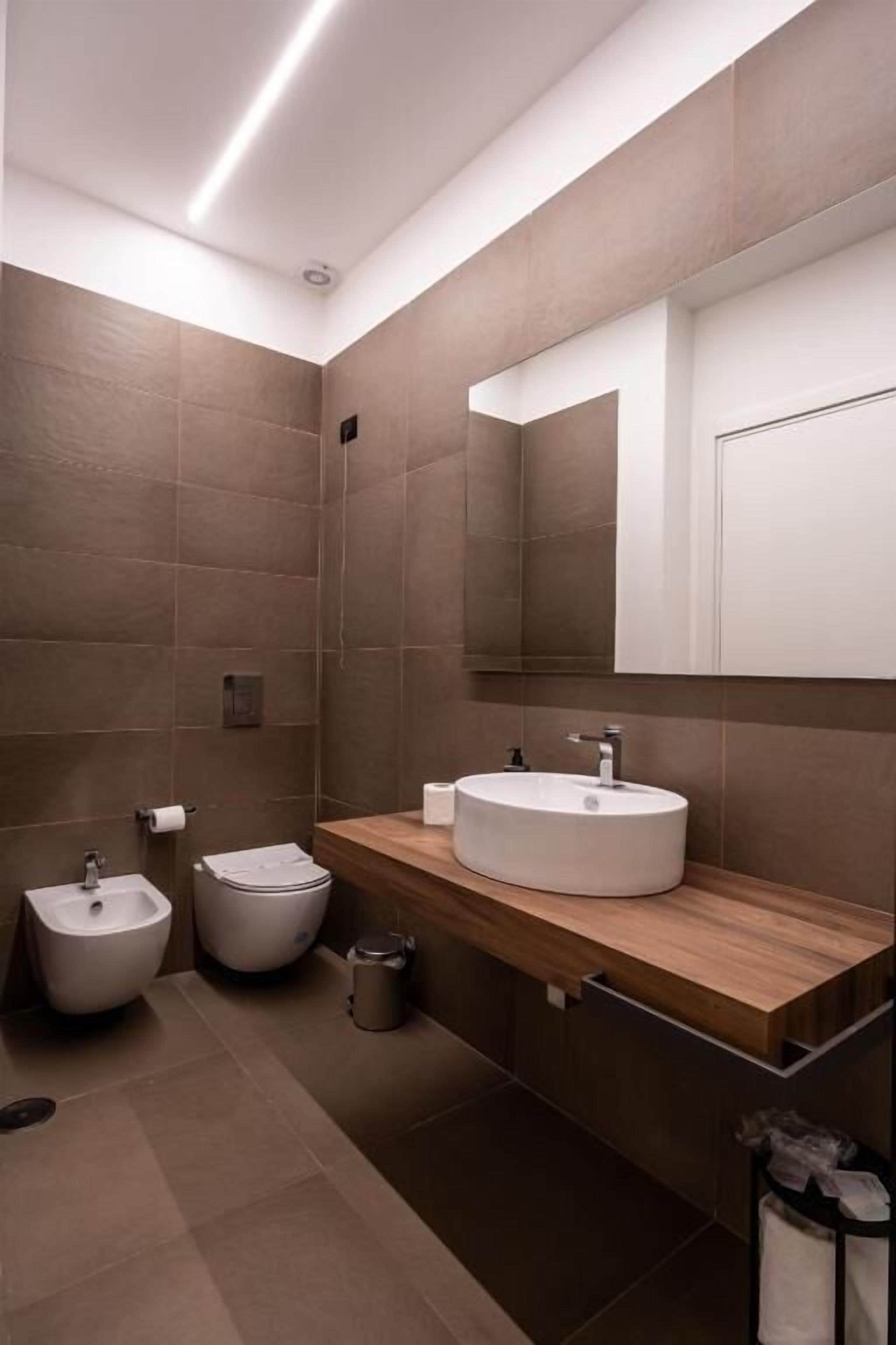 Une salle de bain moderne avec un grand miroir, un lavabo rond et deux bidet.