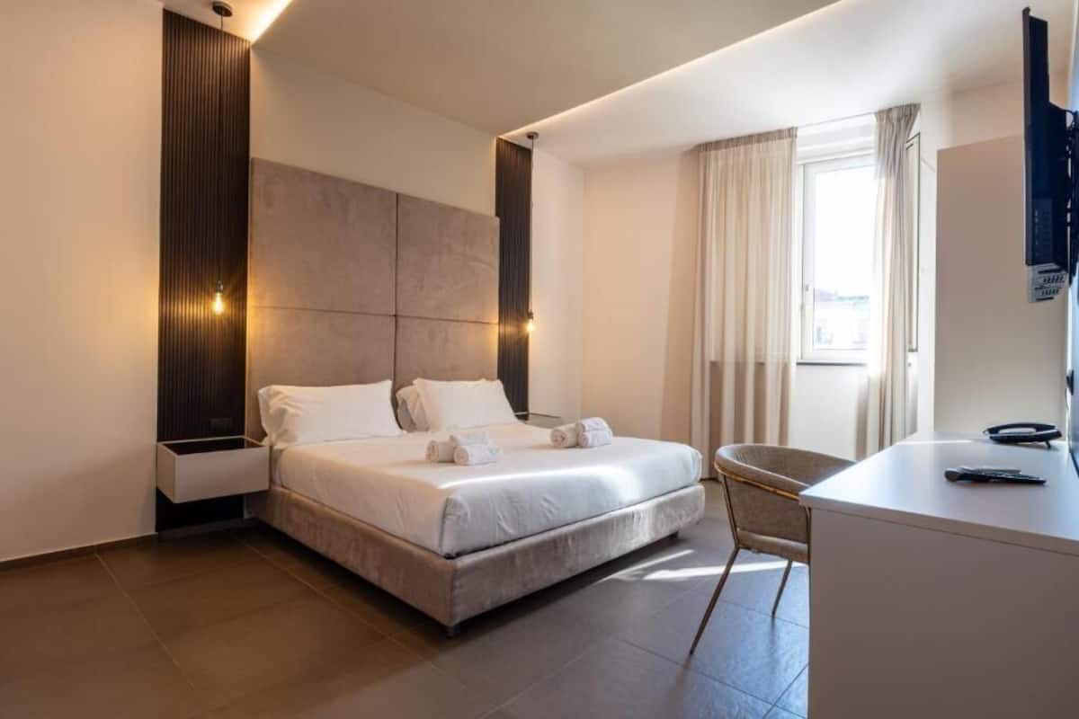 A modern hotel room with a large bed, a desk, and a chair.