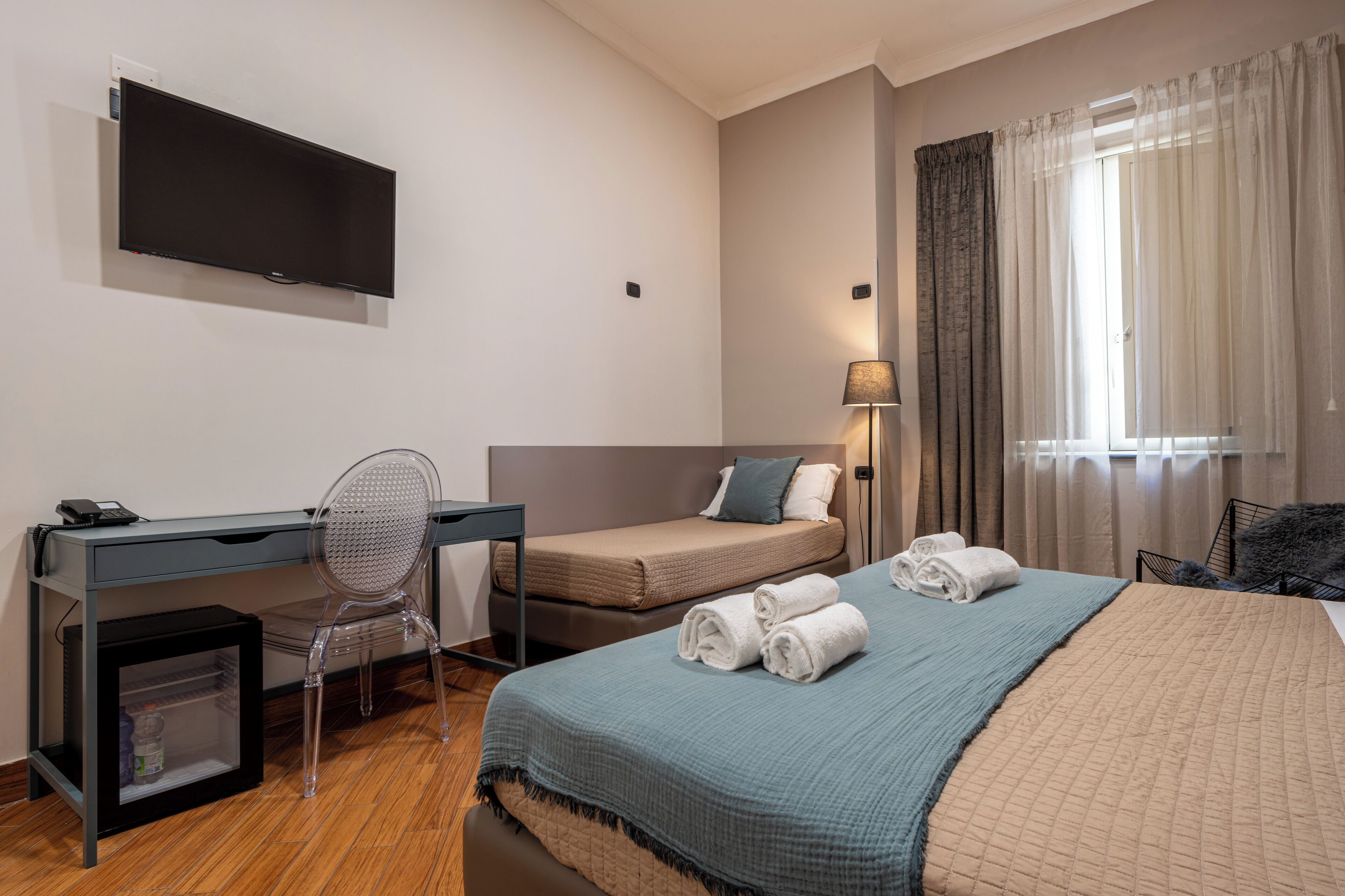 A hotel room with a bed, a desk, a chair, a TV, and a window with curtains.