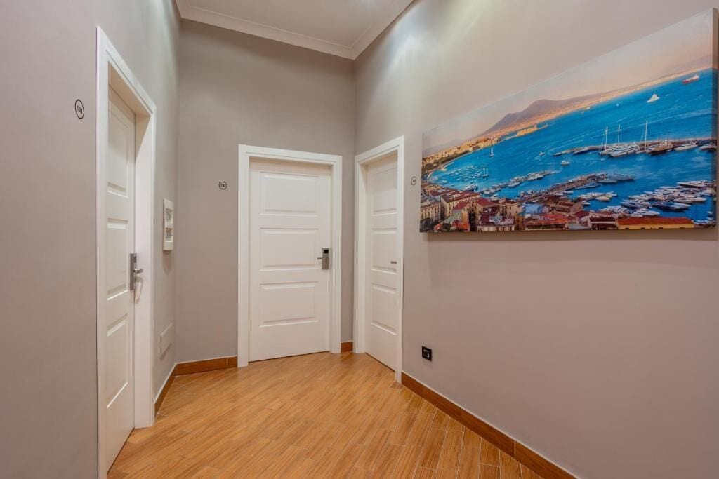 Un pasillo con suelo de madera, puertas blancas y un cuadro de una escena costera.