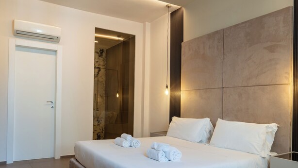 A modern hotel room with a large bed, a walk-in shower, and a minimalist design.