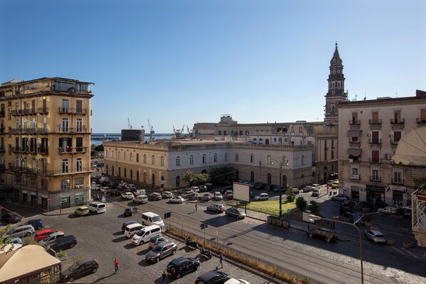 Una plaza urbana con edificios históricos, una imponente torre del reloj y una calle concurrida con automóviles y peatones.