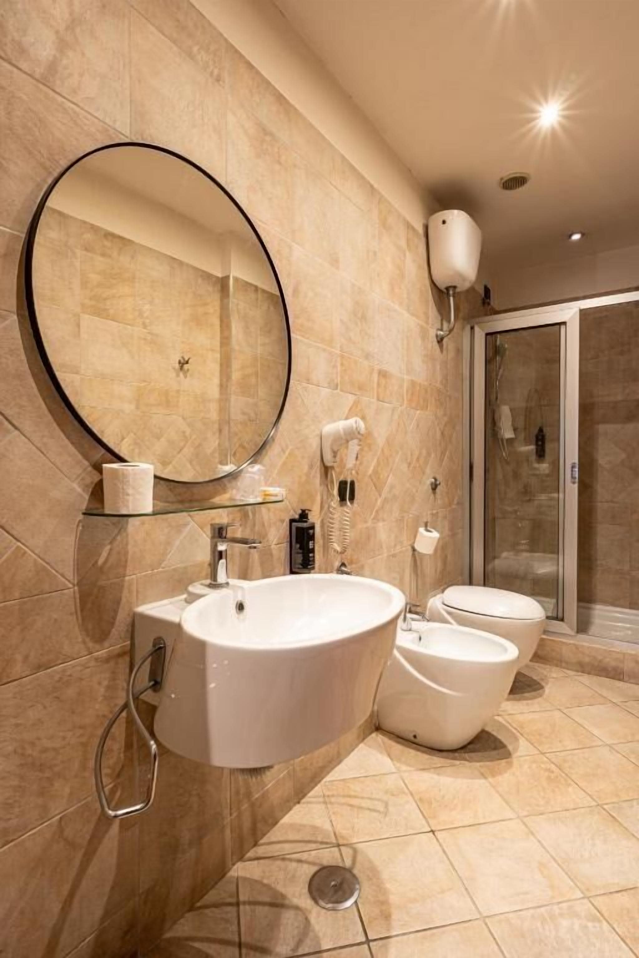 Une salle de bain moderne avec un grand miroir, un lavabo, deux toilettes et une douche à parois de verre.