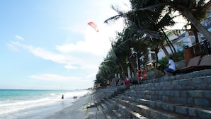 A beach with stone steps leading down to the water, palm trees, and a lifebuoy on the railing. - Novela Muine Resort & Spa (Mui Ne)