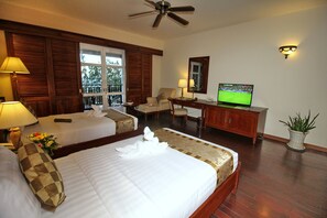 A hotel room with two beds, a desk with a television, a ceiling fan, and a potted plant. - Novela Muine Resort & Spa (Mui Ne)
