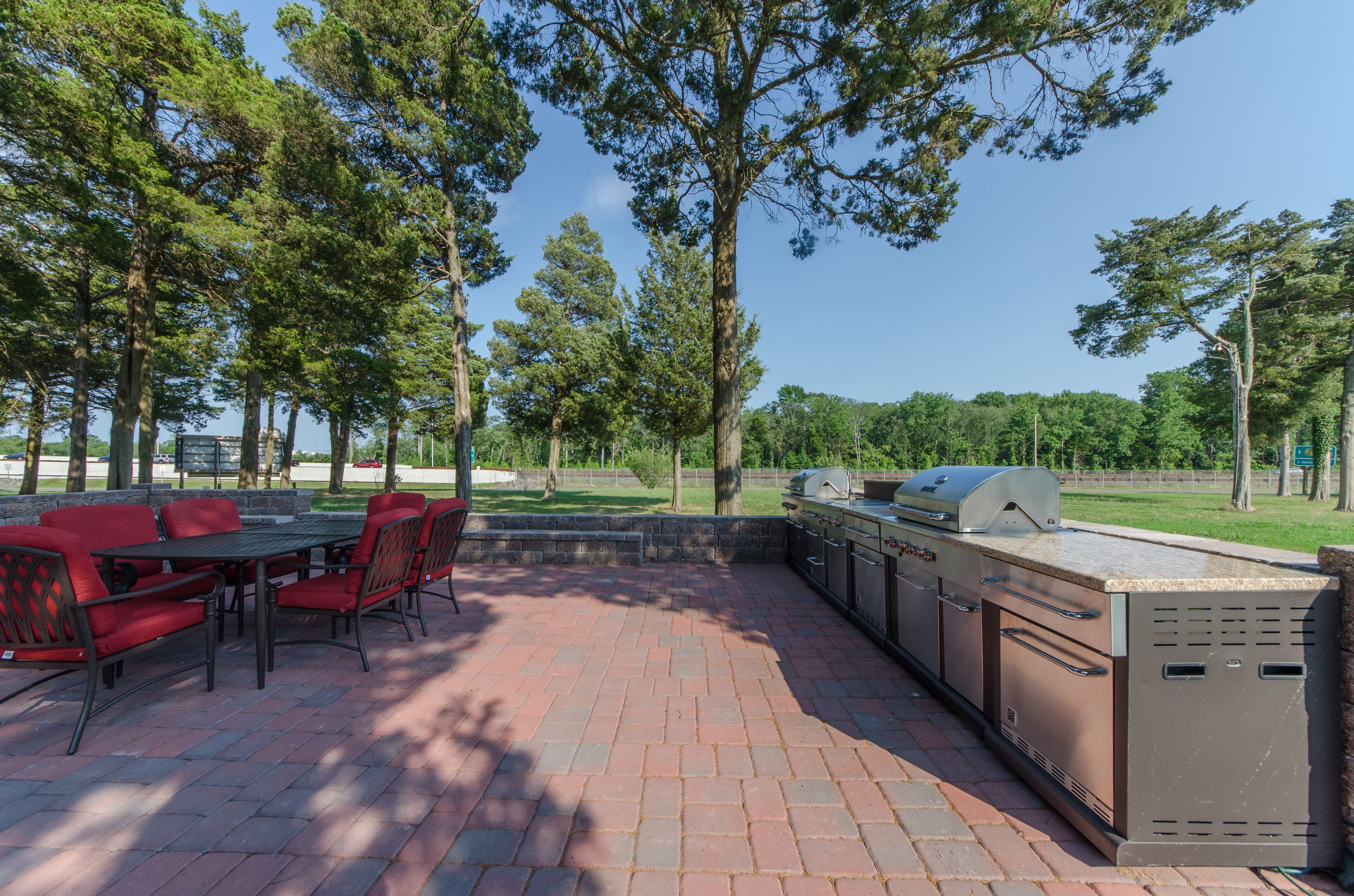An outdoor patio with a brick floor, red chairs, and a built-in grill station.