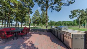 An outdoor patio with a brick floor, red chairs, and a built-in grill station.