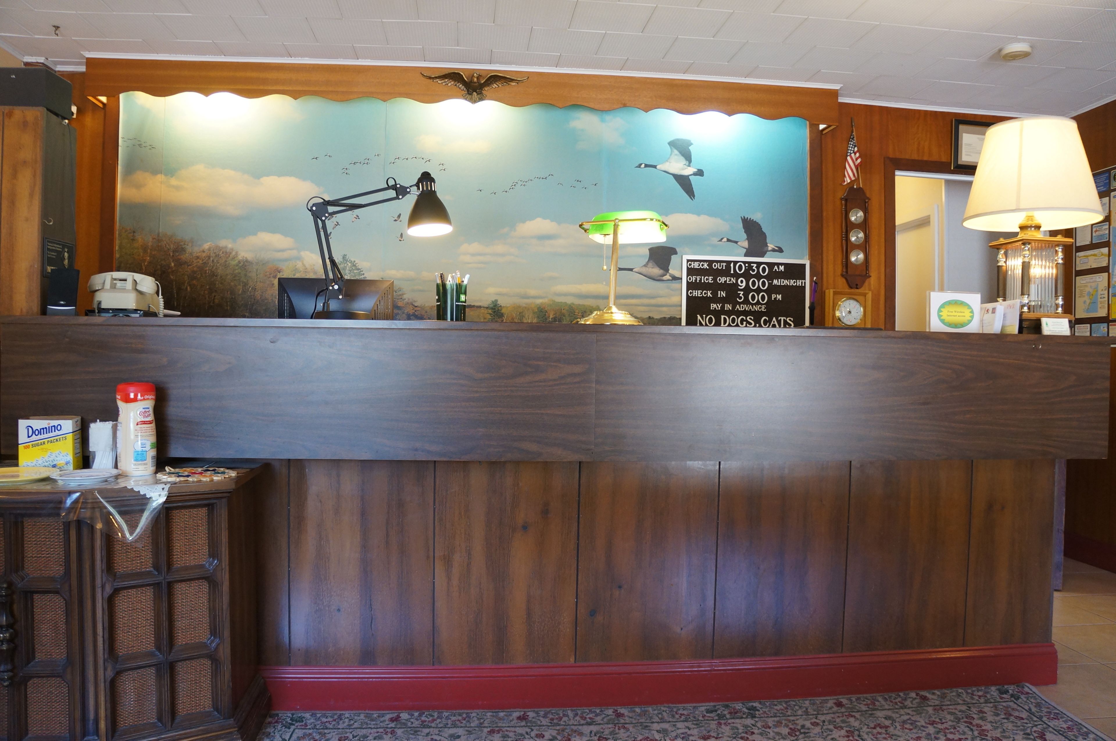 A wooden reception desk with a mural of birds in flight, a clock, and a sign with office hours.