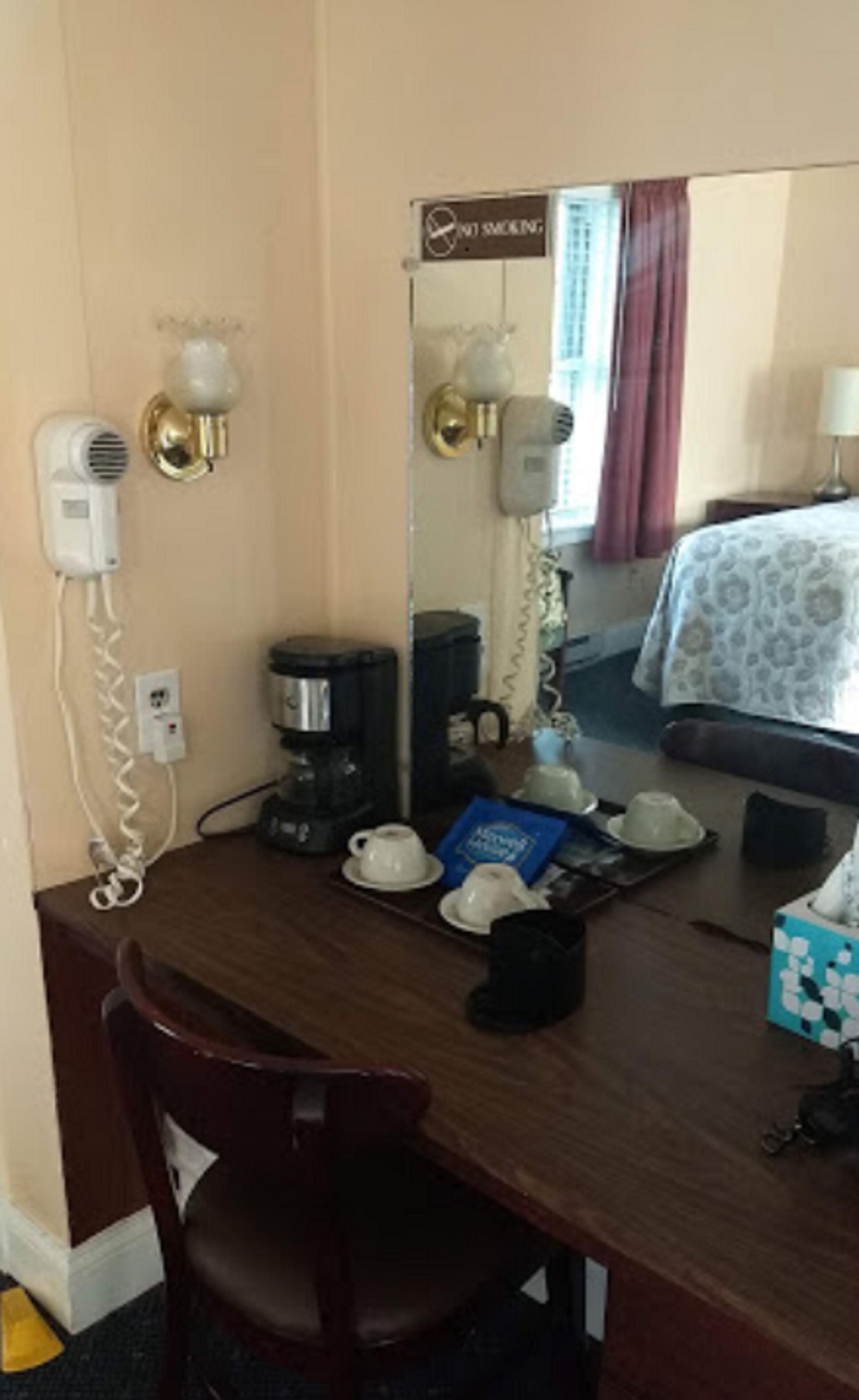 A hotel room with a wooden desk, a hairdryer, a coffee maker, and a mirror.
