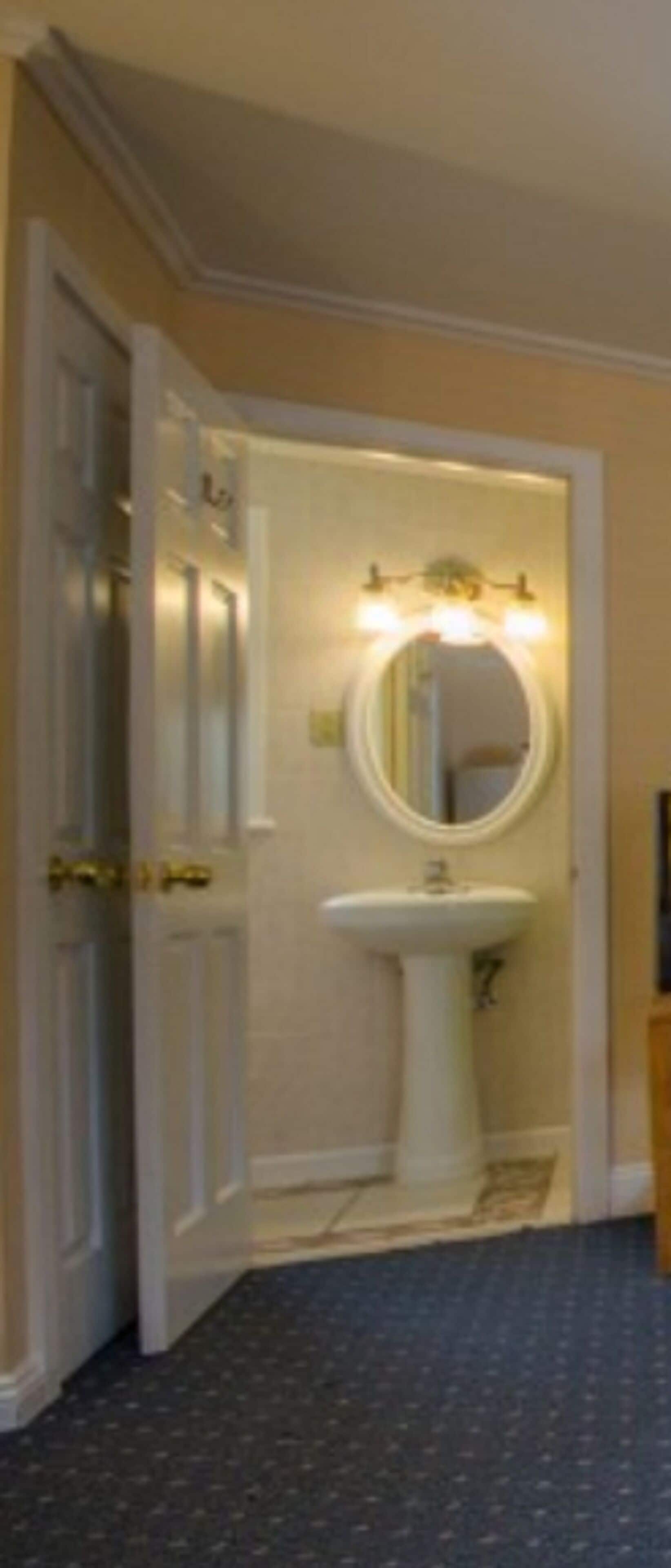A bathroom with a pedestal sink, a round mirror, and a light fixture above the mirror.