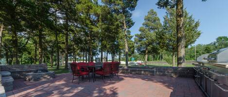 An outdoor patio with a brick floor, red chairs, and a barbecue grill.
