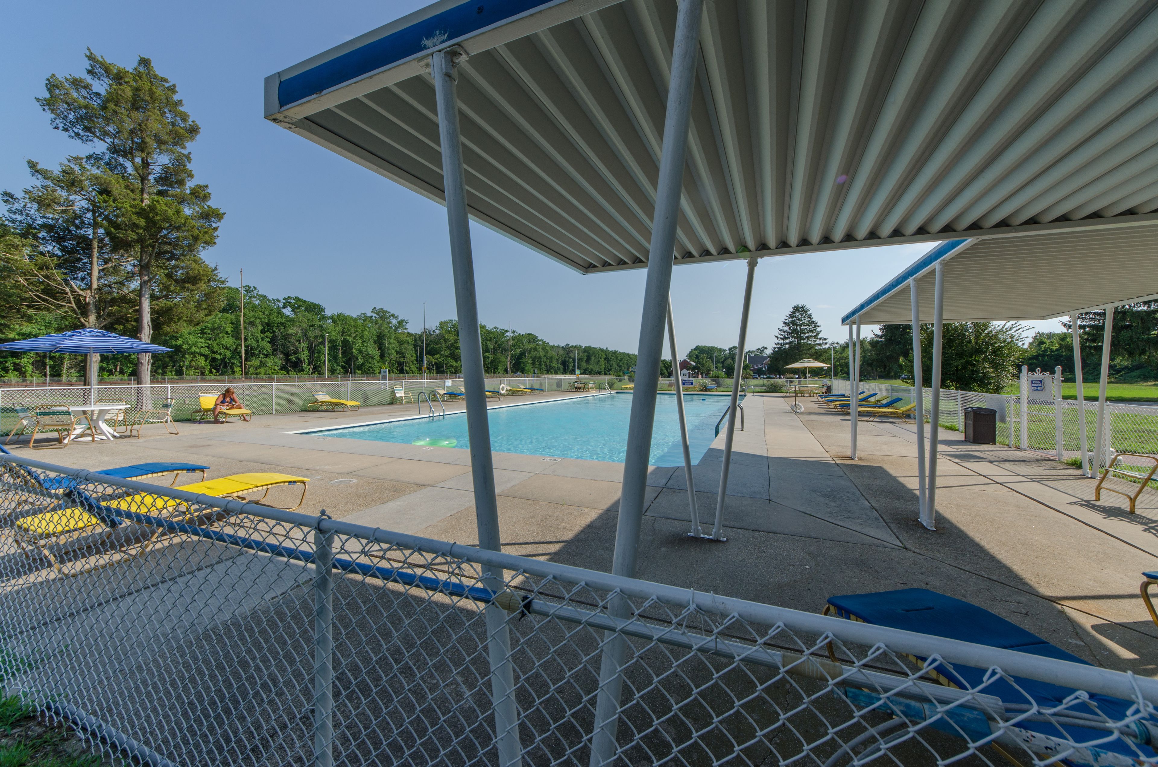 A covered outdoor swimming pool area with lounge chairs and umbrellas.