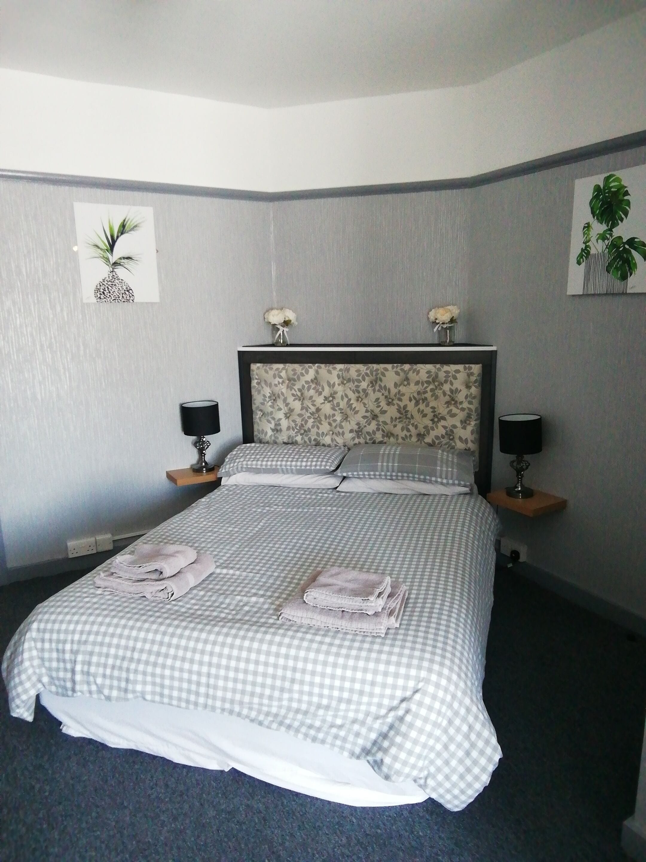 Una cama bien tendida con ropa de cama a cuadros, dos lámparas de noche y un cabecero floral.
