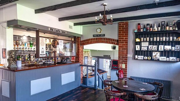 A bar area with a counter, stools, and a wall of bottles. - The Old Castle (Weymouth)