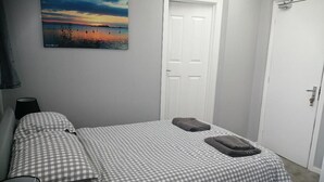 A bedroom with a checkered bedspread, two towels on the bed, a painting on the wall, and a white door. - The Old Castle (Weymouth)