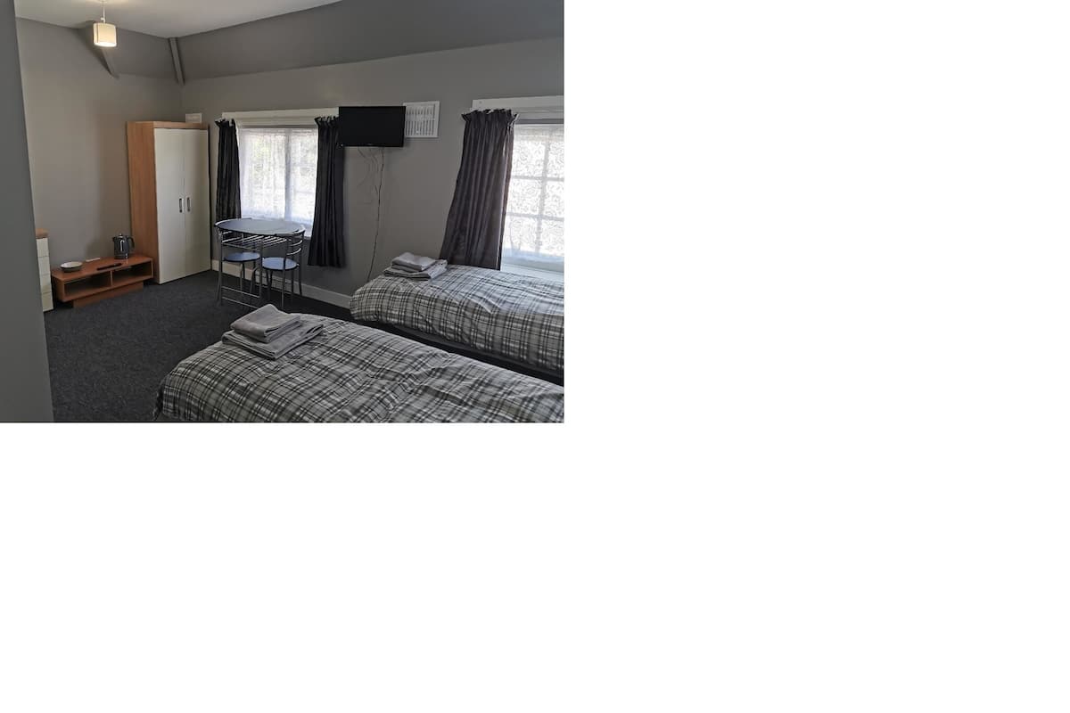 A hotel room with two beds, a desk, a chair, a TV, and a window with curtains.