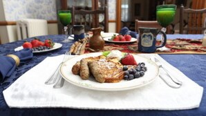 Desayuno con tortitas, fresas, arándanos y un jarro de jugo verde sobre una mesa con mantel azul.