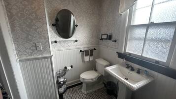 A bathroom with a toilet, sink, and mirror. There is a patterned wallpaper and a window with frosted glass.
